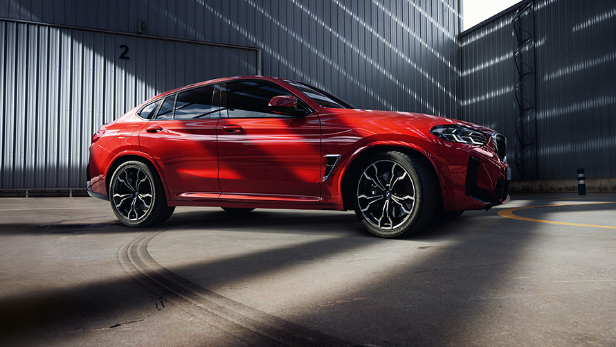 Imagine din partea laterală a unui BMW X4 M F98 LCI Facelift 2021 Roşu Toronto în faţa unei fabrici