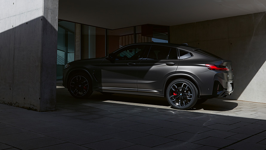 Imagine din partea laterală a unui BMW X4 M40i G02 LCI 2021 Facelift, aflat pe jumătate la umbră în faţa unei case
