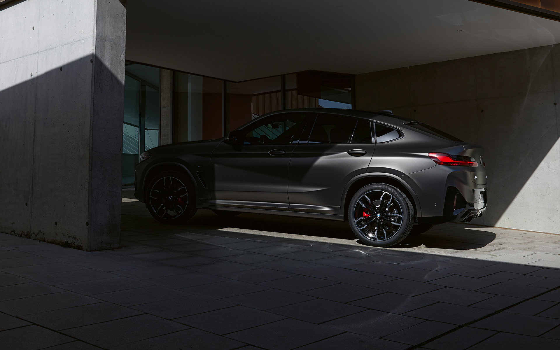 Imagine din partea laterală a unui BMW X4 M40i G02 LCI 2021 Facelift, aflat pe jumătate la umbră în faţa unei case