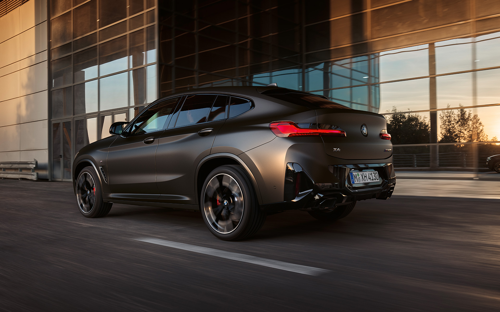 Imagine cu trei sferturi din partea din spate a unui BMW X4 M40i G02 LCI 2021 Facelift în faţa unei faţade din sticlă