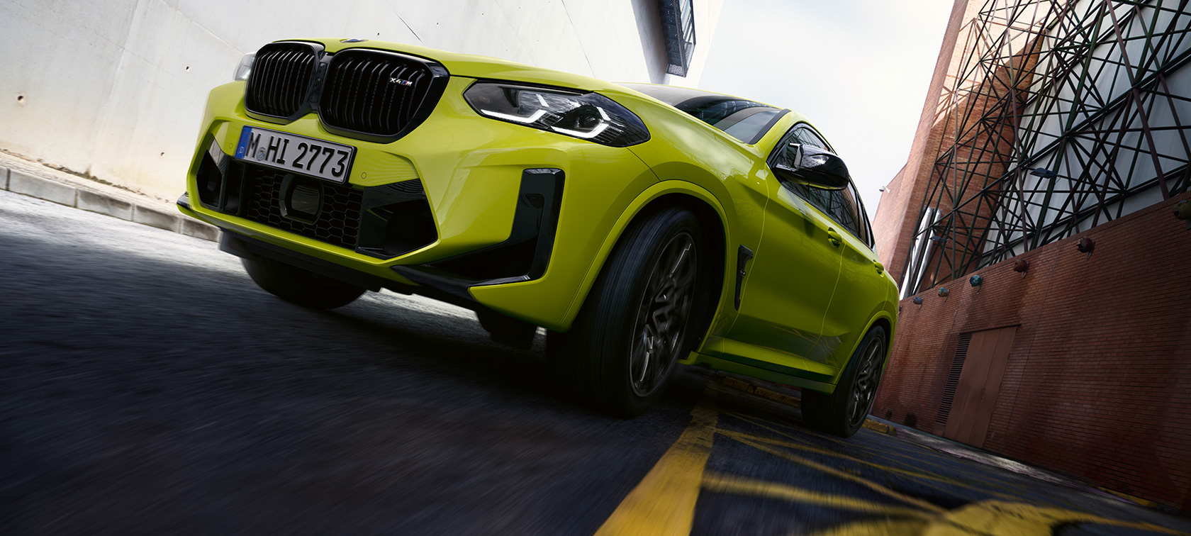 Imagine cu trei sferturi din partea frontală şi imagine din partea de jos a unui BMW X4 M Competition F98 LCI 2021 Imagine cu trei sferturi din partea frontală şi imagine din partea de jos a unui BMW X4 M Competition F98 LCI Facelift 2021 Galben Sao Paulo în timp ce se deplasează printr-un cartier plin de case
