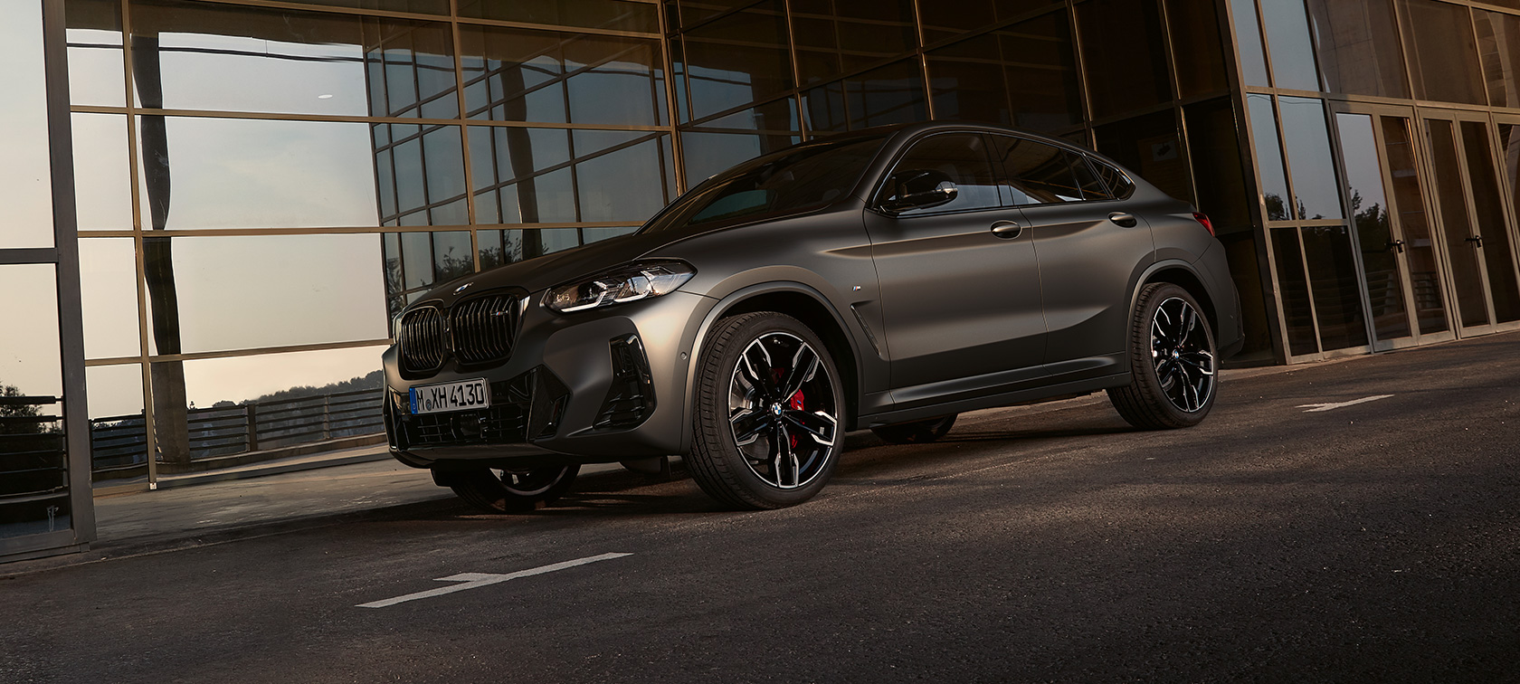 Imagine cu trei sferturi din partea frontală a unui BMW X4 M40i G02 LCI 2021 Facelift Imagine cu trei sferturi din partea frontală a unui BMW X4 M40i G02 LCI 2021 Facelift în dreptul unei faţade din sticlă