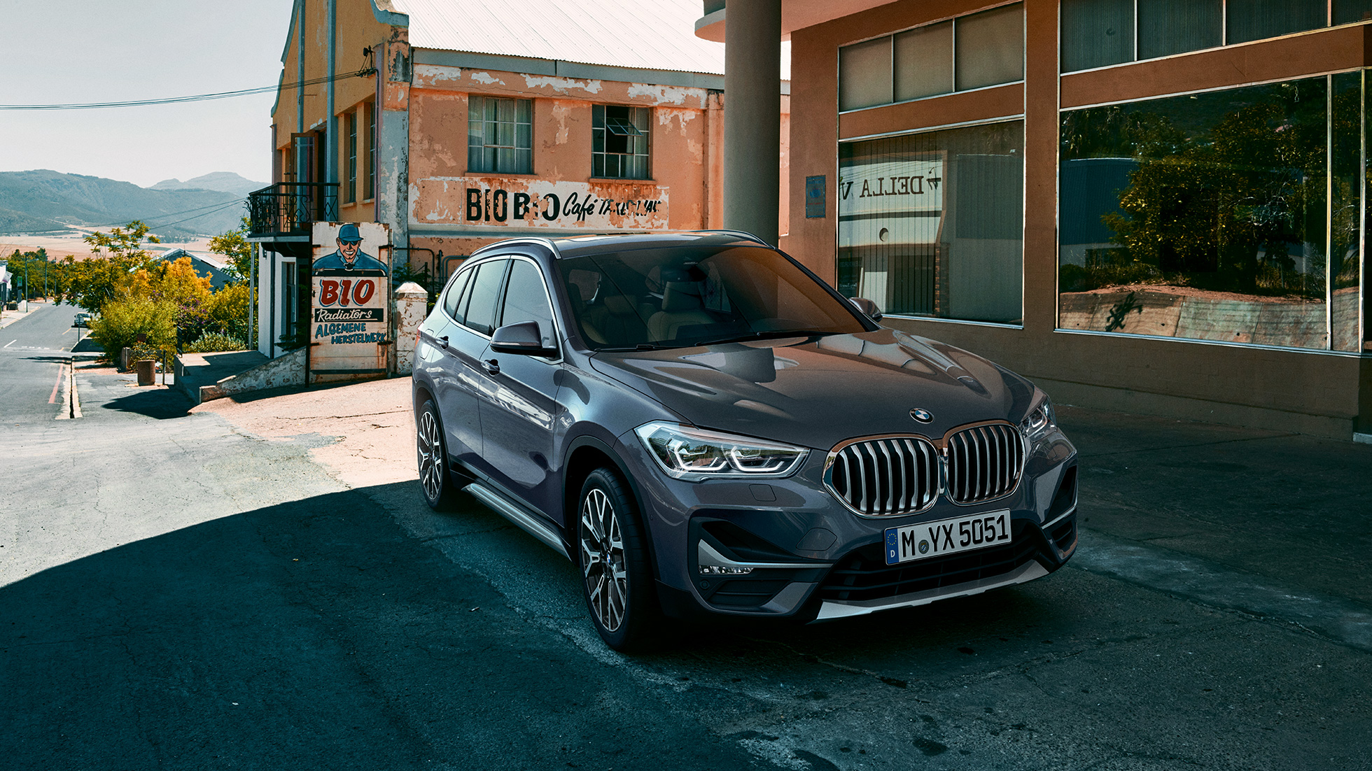 Imagine cu trei sferturi din partea frontală a BMW X1. Imagine cu trei sferturi din partea frontală a BMW X1 staţionând în faţa unui peisaj urban.