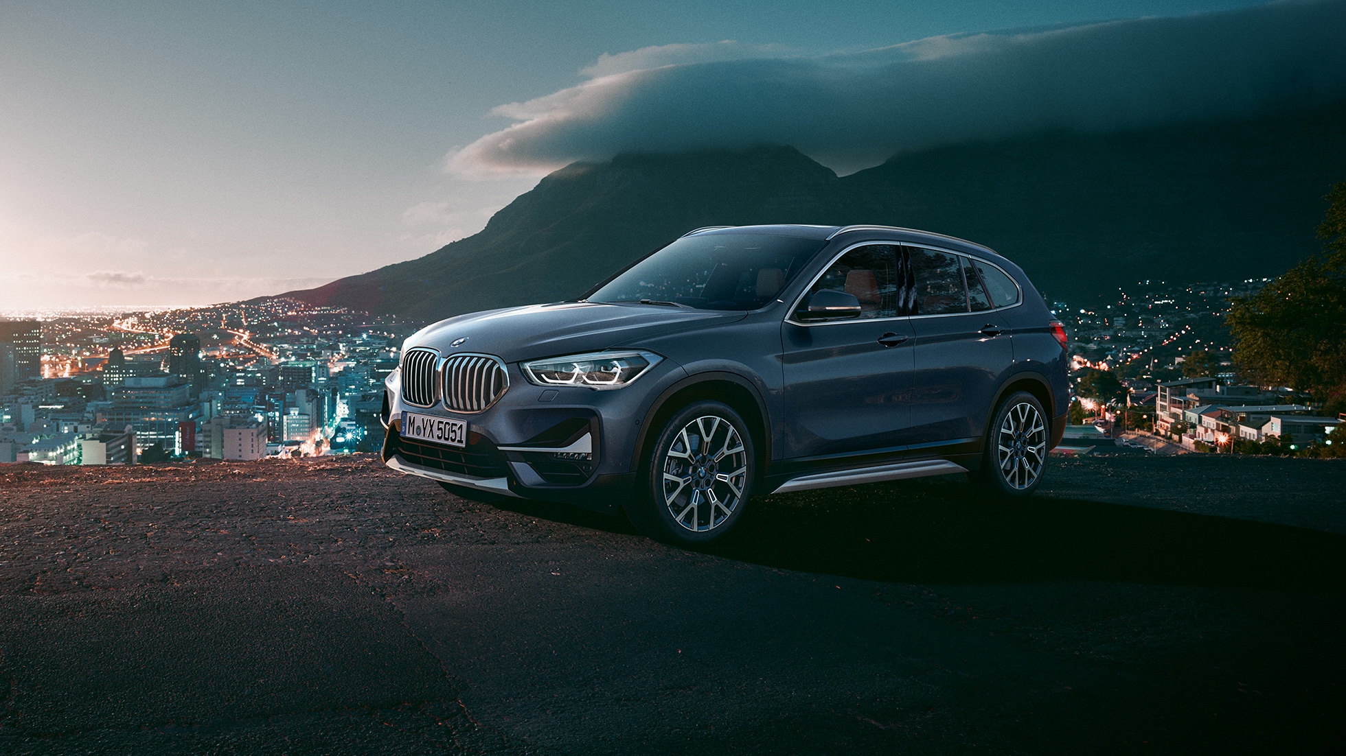Imagine cu trei sferturi din partea laterală a BMW X1. Imagine cu trei sferturi din partea laterală a BMW X1 staţionând în faţa unui peisaj urban.