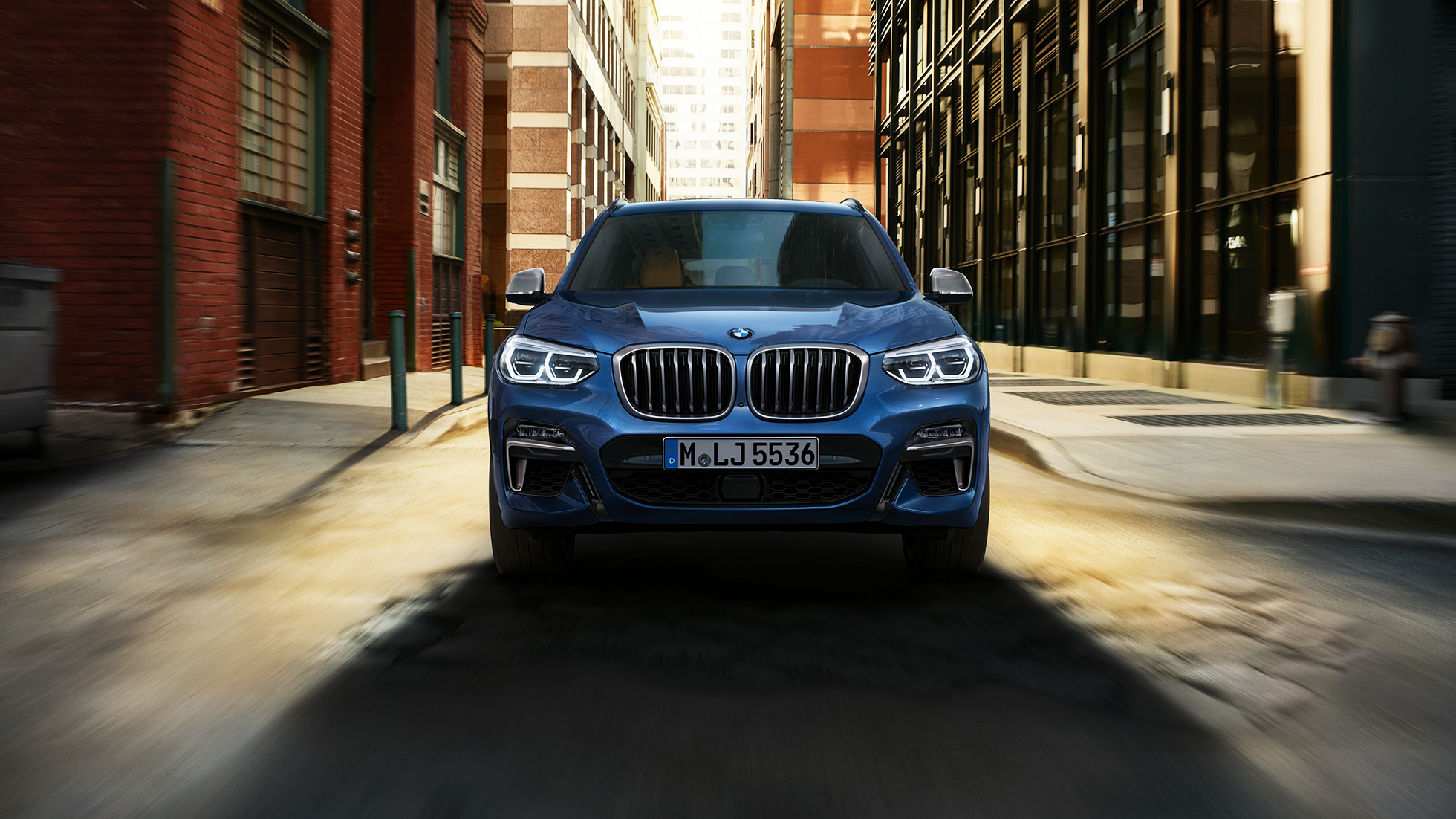Imagine cu partea frontală a BMW X3 M40i în faţa unui peisaj urban Imagine cu partea frontală a BMW X3 M40i în faţa unui peisaj urban