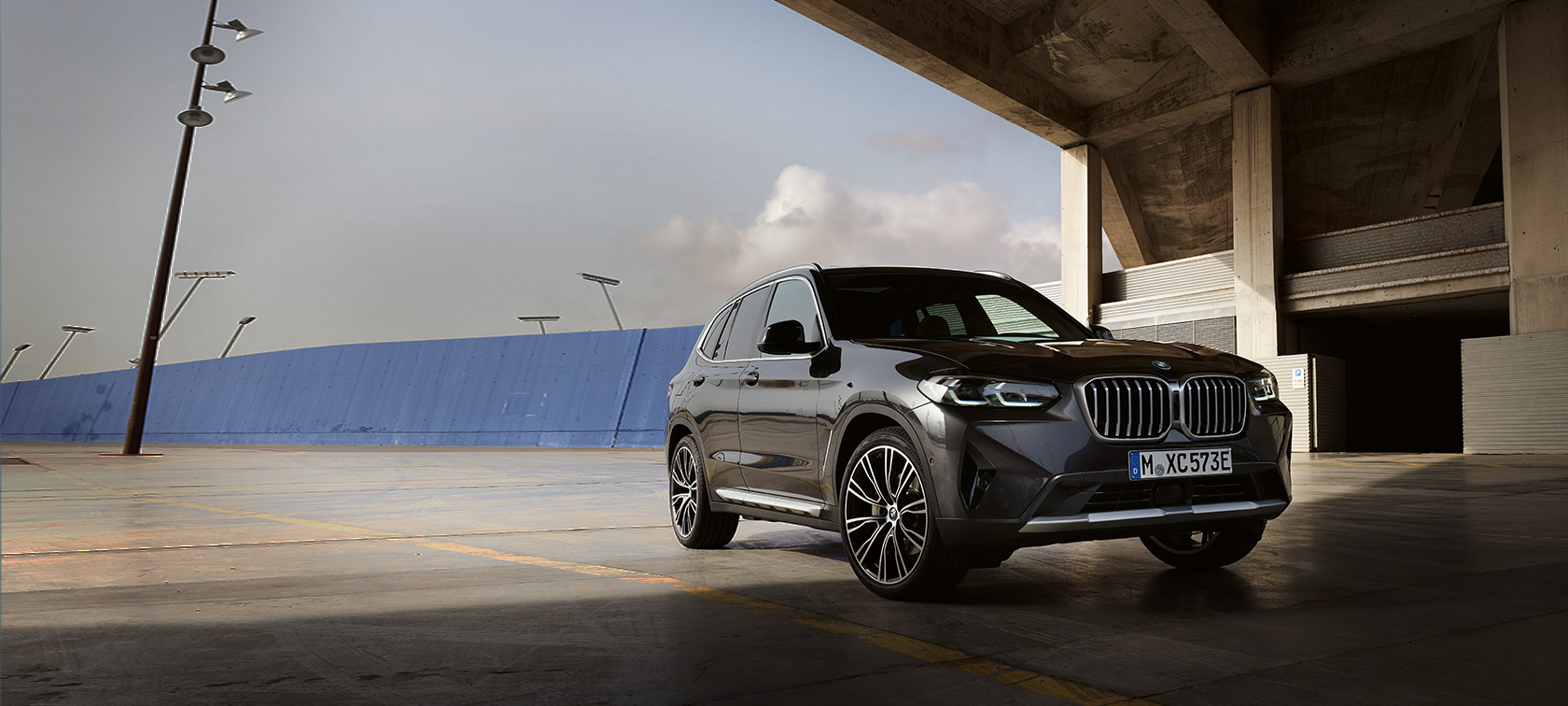 Imagine cu trei sferturi din partea frontală a BMW X3 G01 2021 în Gri Sophisto, în faţa unui hangar
