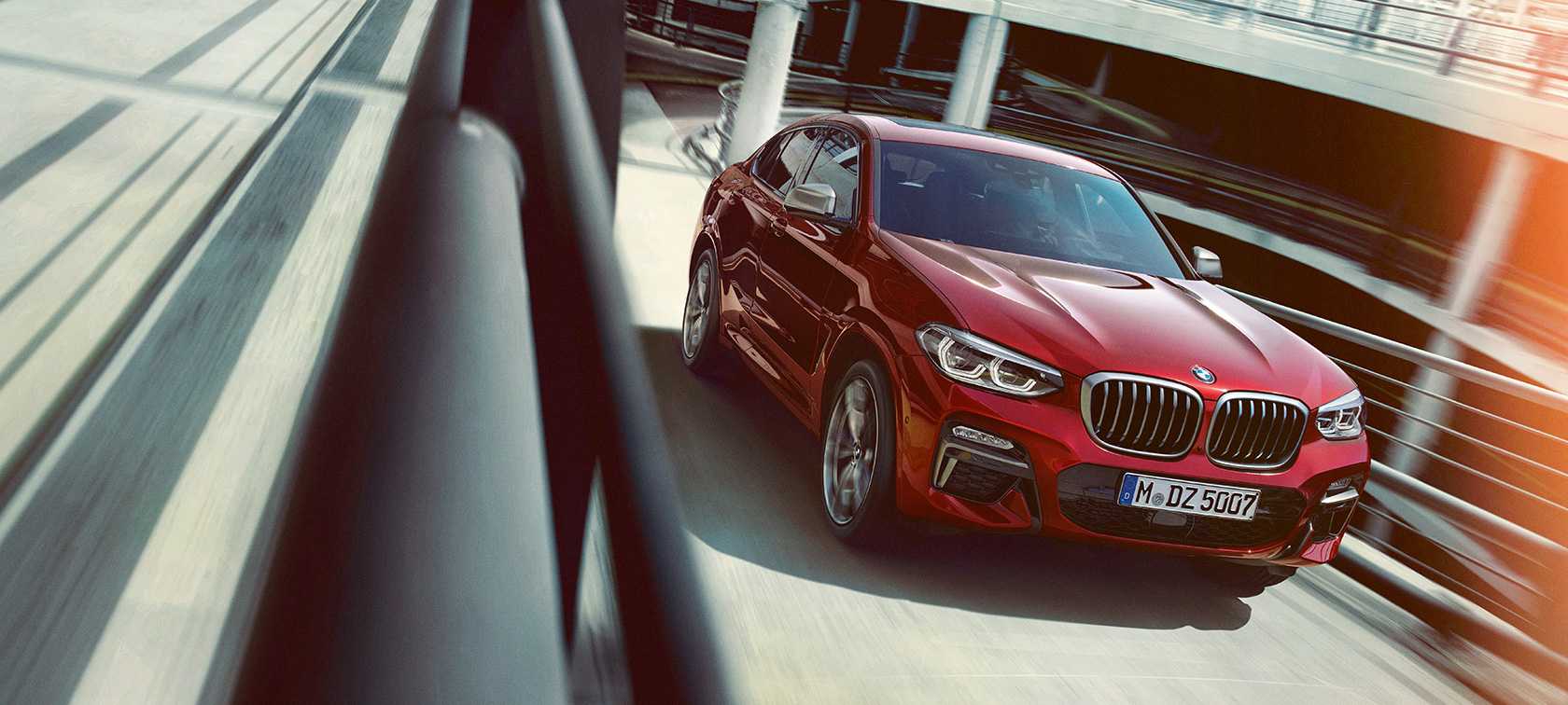 BMW X4 rulând într-o parcare supraetajată Imagine cu trei sferturi din partea laterală a BMW X4, G02, 2018, în Roşu Flamenco Brilliant Effect, rulând într-o parcare supraetajată
