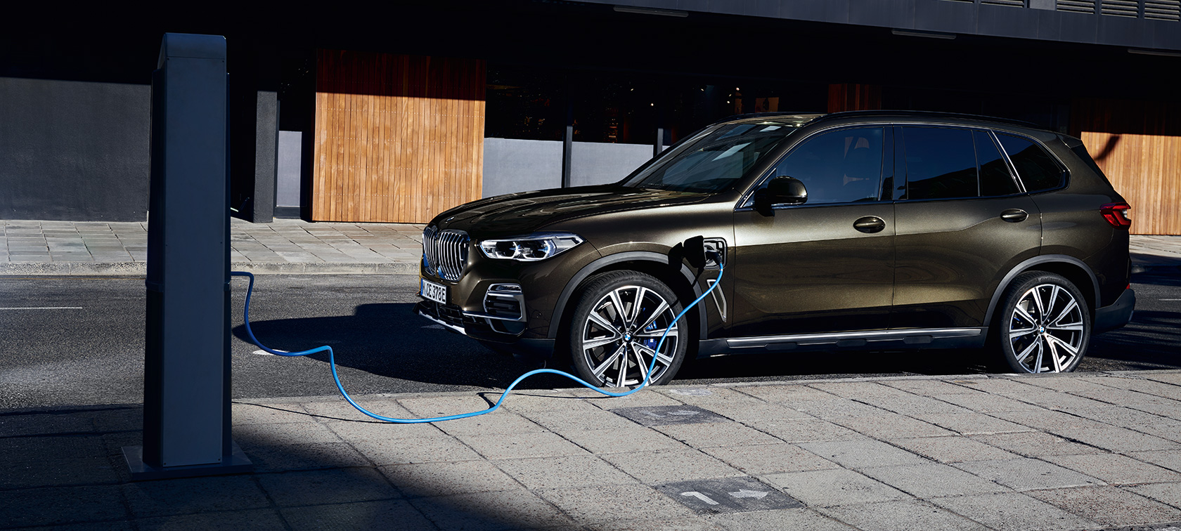 Imagine cu trei sferturi din partea laterală a automobilului BMW X5 xDrive45e G05 plug-in hybrid Imagine cu trei sferturi din partea laterală a automobilului BMW X5 xDrive45e G05 plug-in hybrid în timp ce se încarcă