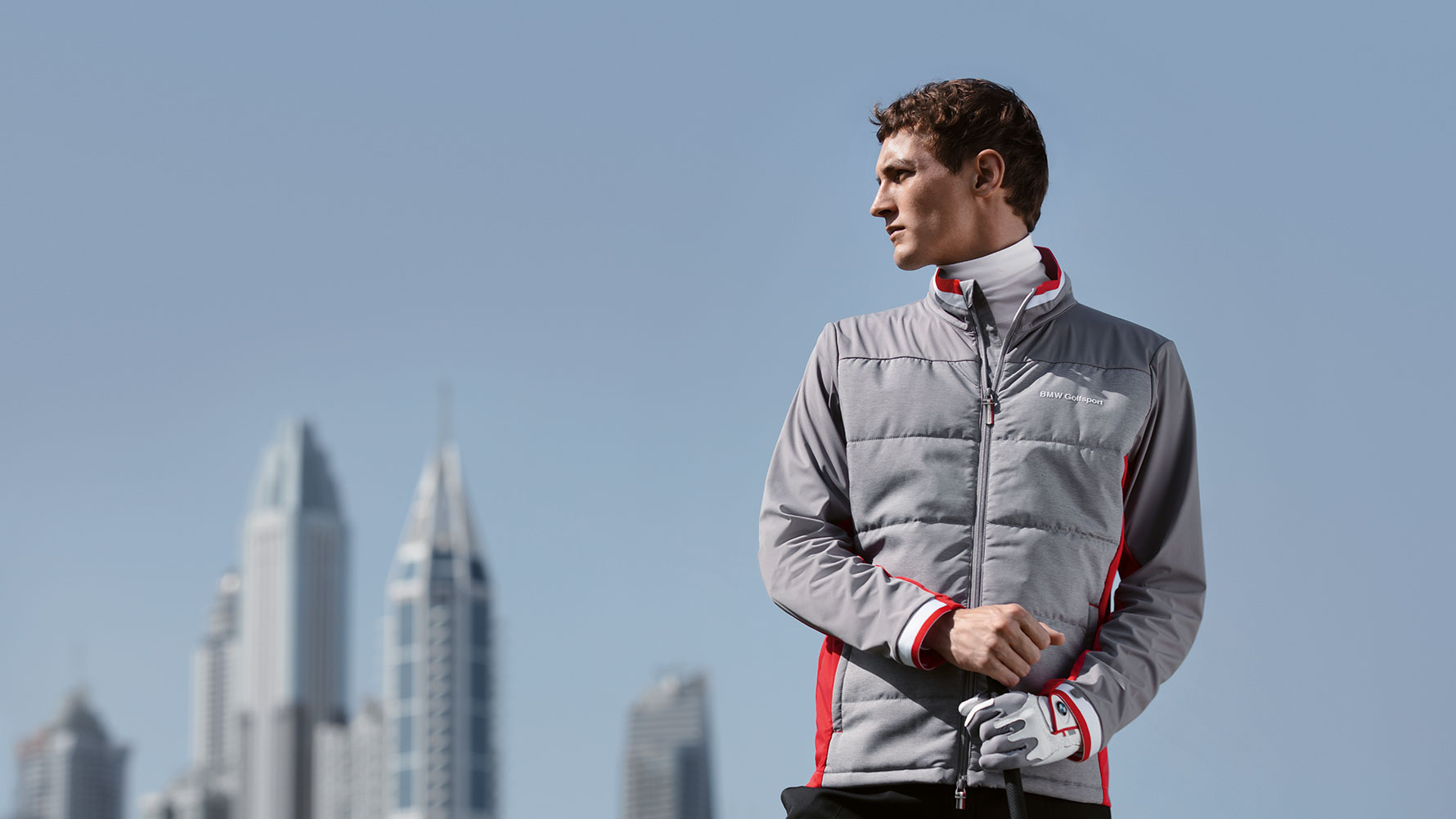 Un model masculin prezintă produse din Colecţia BMW Golfsport cu orizontul unui oraş mare pe fundal. Un model masculin prezintă produse din Colecţia BMW Golfsport cu orizontul unui oraş mare pe fundal.