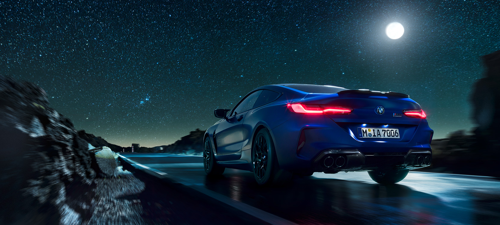 Imagine cu partea spate a BMW M8 Competition Coupé. Imagine cu partea spate a BMW M8 Competition Coupé rulând noaptea cu lună plină.