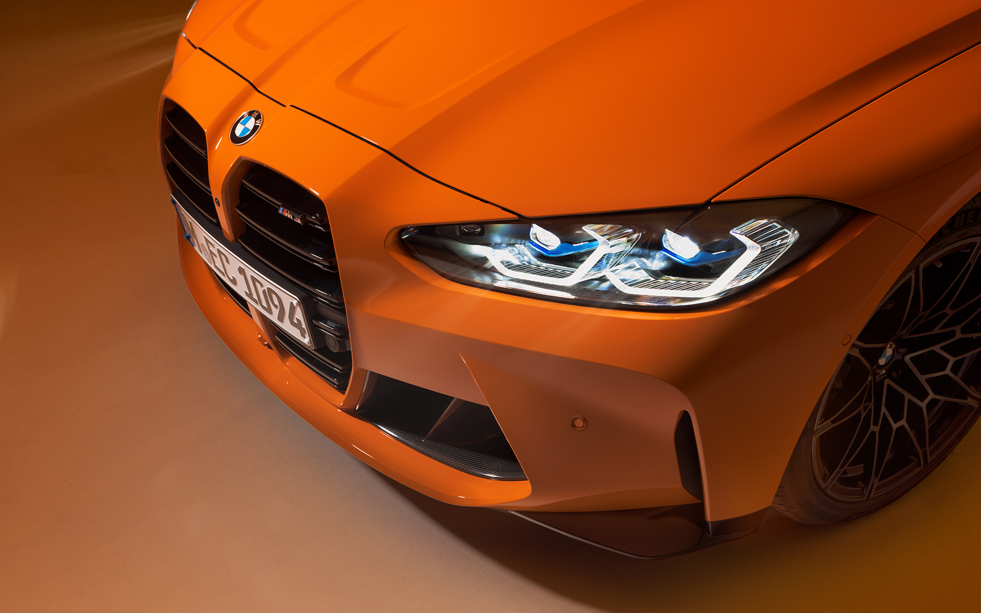Imagine cu trei sferturi din partea frontală a BMW M4 Competition Coupé G82 2021, BMW Individual Portocaliu Fire staţionând, prim plan cu perspectivă de sus
