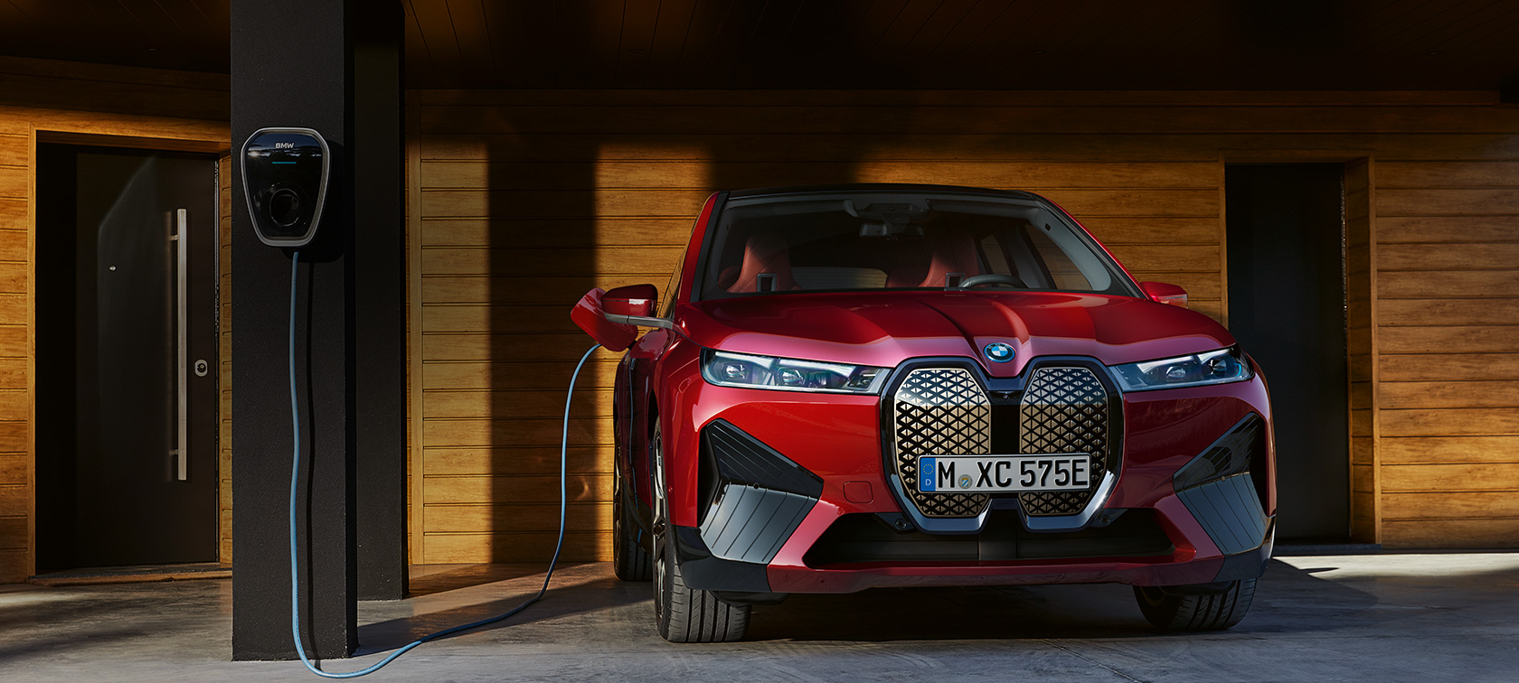 Imagine din partea frontală a unui BMW iX conectat la sistemul Wallbox de acasă Imagine din partea frontală a unui BMW iX conectat la sistemul Wallbox dintr-un garaj cu panouri din lemn