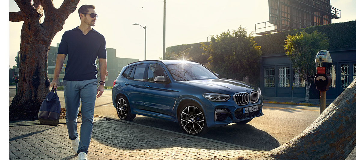 Bărbat cu ochelari de soare în faţa unui BMW albastru Bărbat cu ochelari de soare în faţa unui BMW albastru